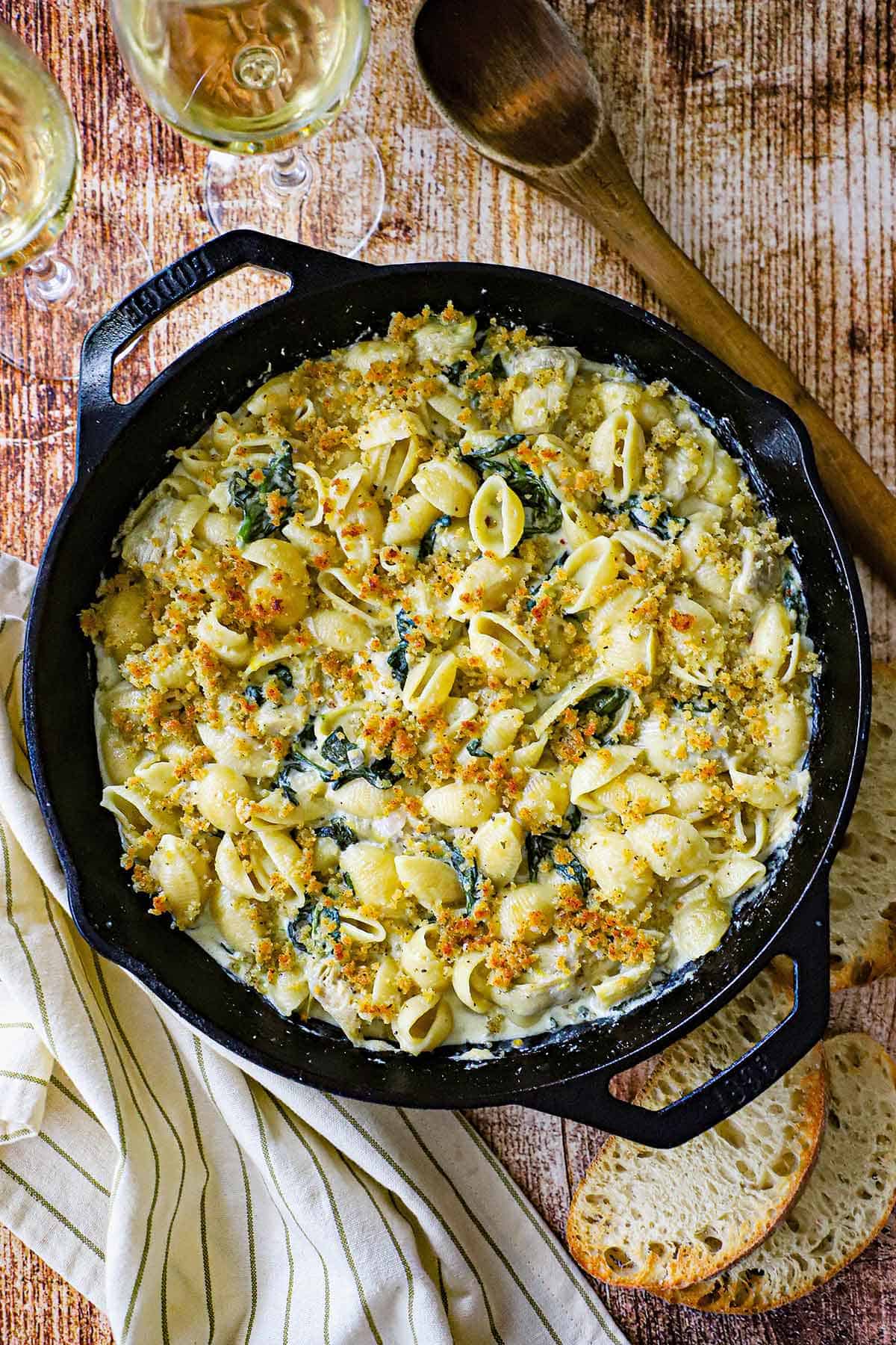 An overhead view of a large cast-iron skillet filled with freshly prepared Spinach Artichoke Dip Pasta topped with a toasty Panko breadcrumb mixture.