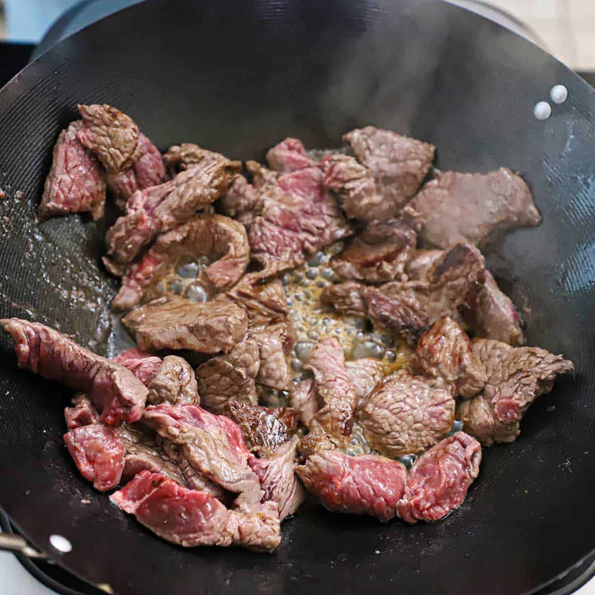 A wok that is filled with chunks of beef tenderloin that are being stir-fried in hot oil.