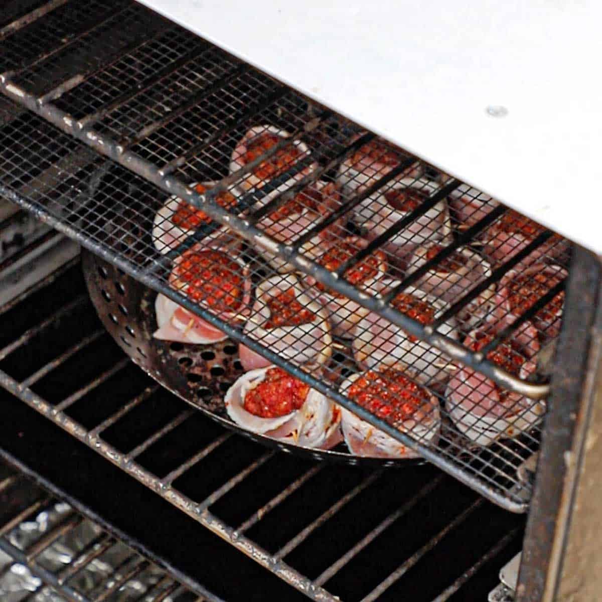 A person placing a perforated grill rack filled with uncooked bacon-wrapped meatballs in an electric smoker.