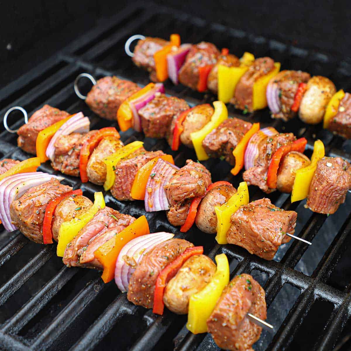 Four steak kabobs being grilled on a gas stove.