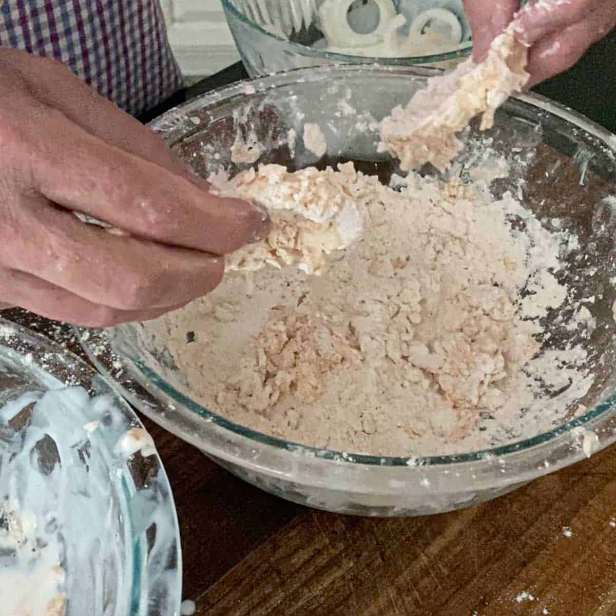 A person dredging a ring of onion through flour a second time after submerging it in buttermilk.