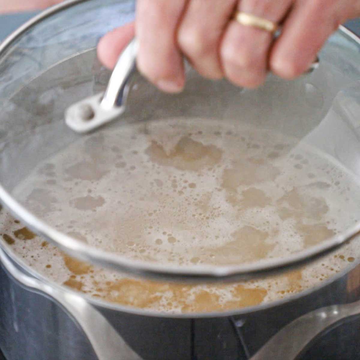 A person placing a clear lid onto a saucepan filled with simmering broth and Jasmine rice.