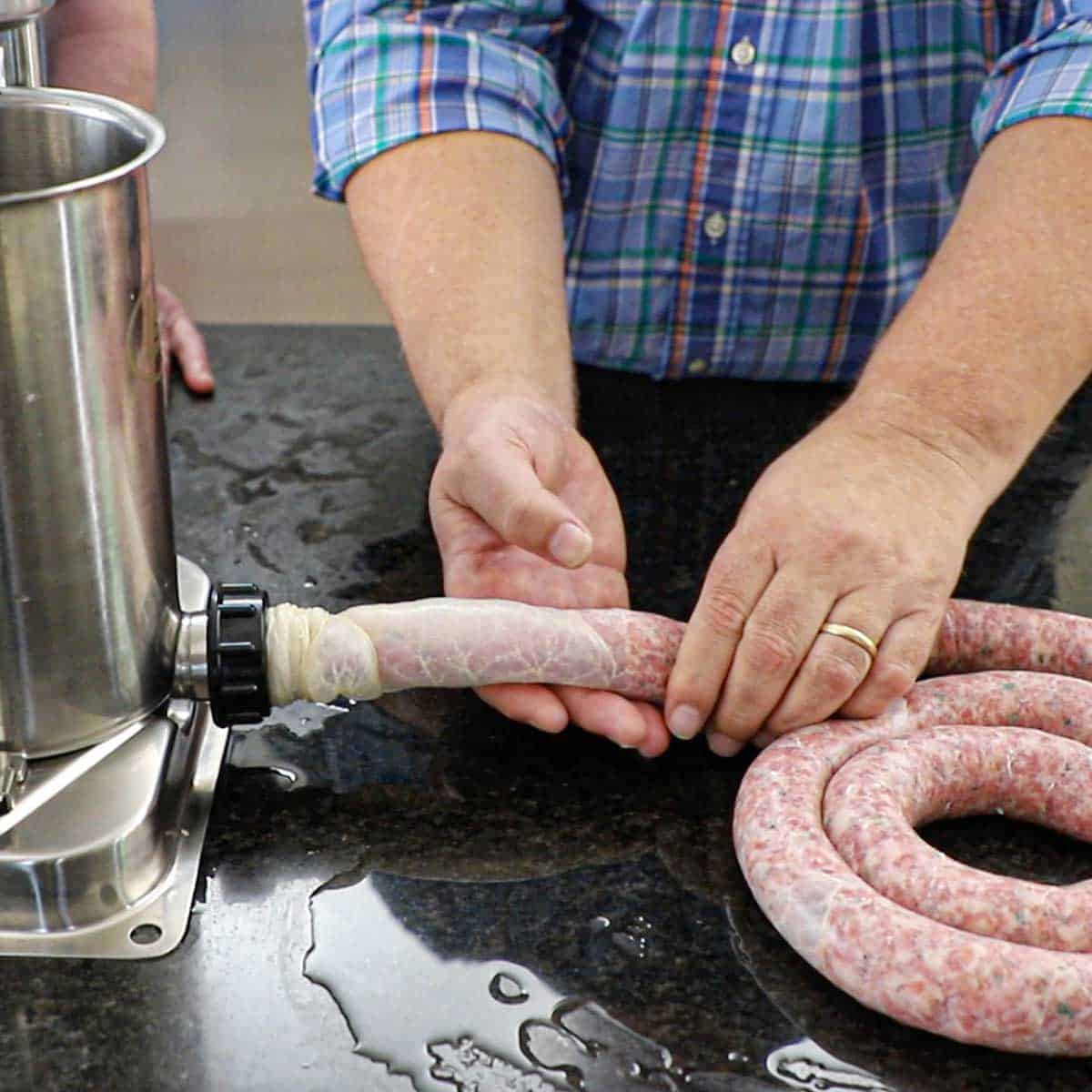 A person using his hands to help guide Italian sausage that is being cranked from a sausage stuffer canister into one long rope that he is shaping into a circular formation.