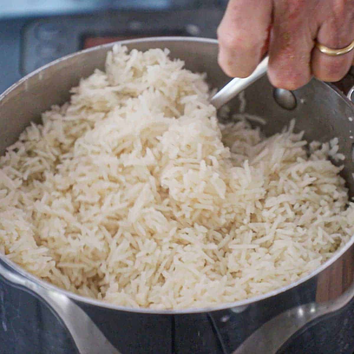 A person using a fork to fluff freshly prepared Peruvian garlic rice in a silver saucepan.