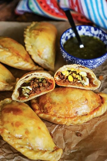 An Argentine Beef Empanada that has been cut in half revealing it beef, green olive, and hard boiled egg filling resting on another whole empanada.