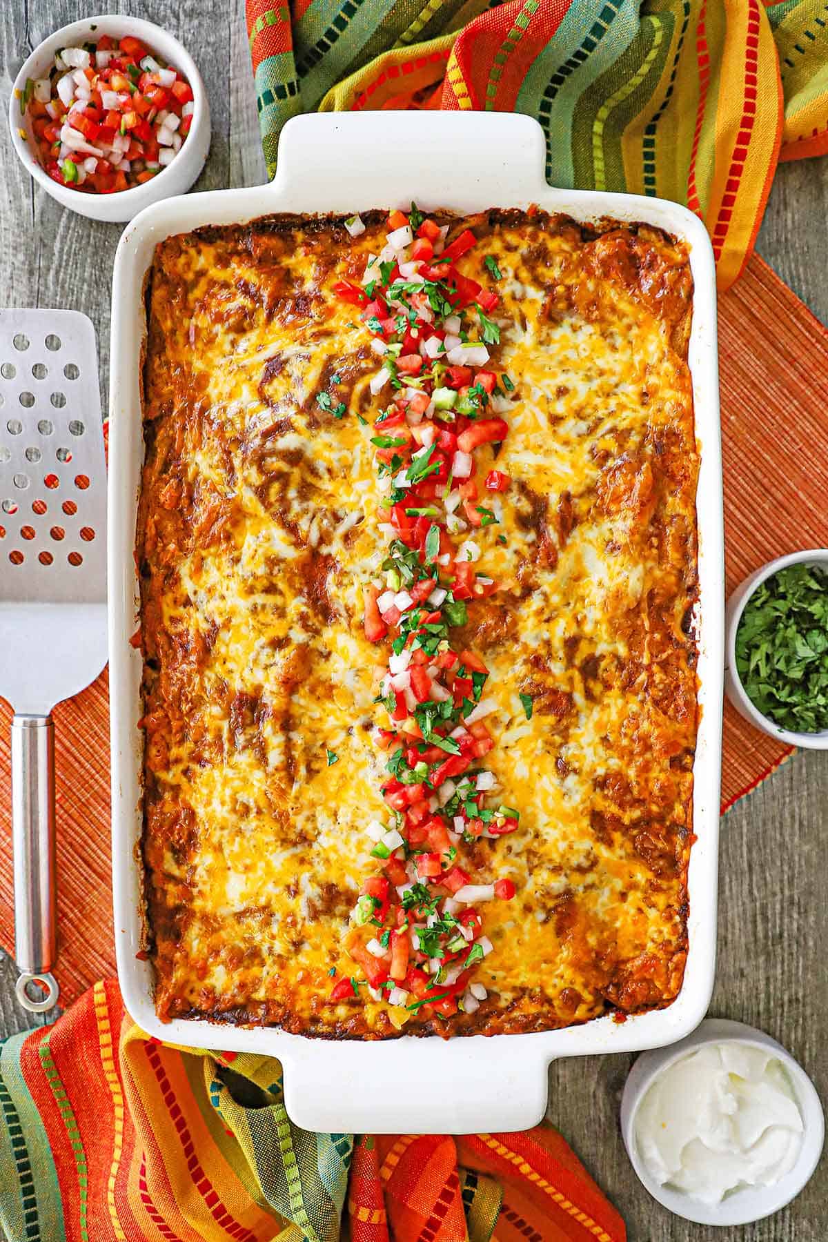 An overhead view of a 9 by 13 inch casserole dish filled with beef enchilada casserole with a row of pico de gallo and chopped cilantro running down the middle of it.