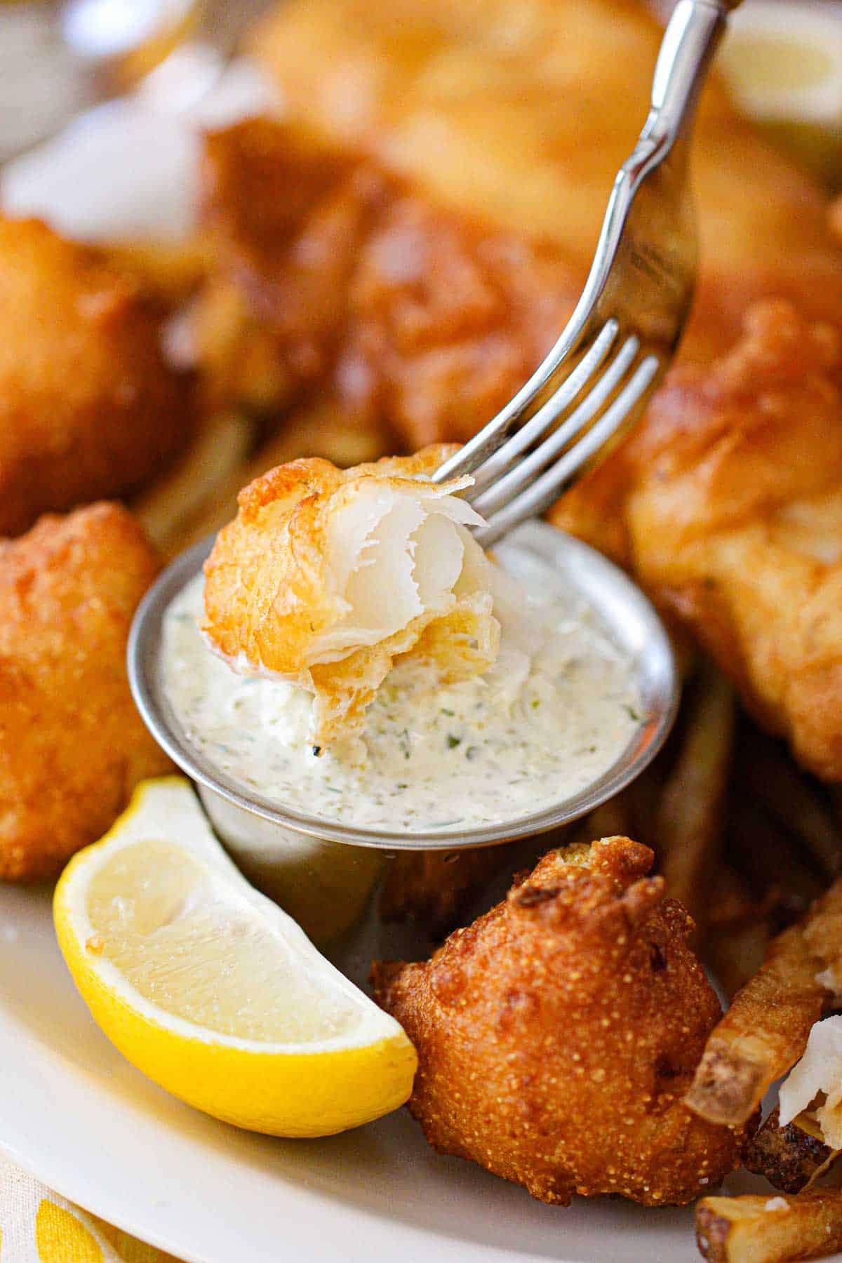 A person using a fork to plunge piece of fried fish into a condiment holder filled with homemade tartar sauce.