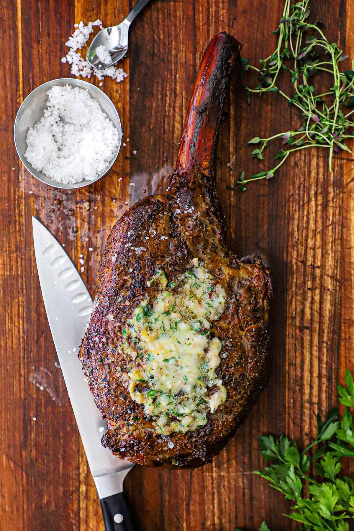An overhead view of a reverse seared tomahawk steak with bone marrow butter that has melted on top of the steak.