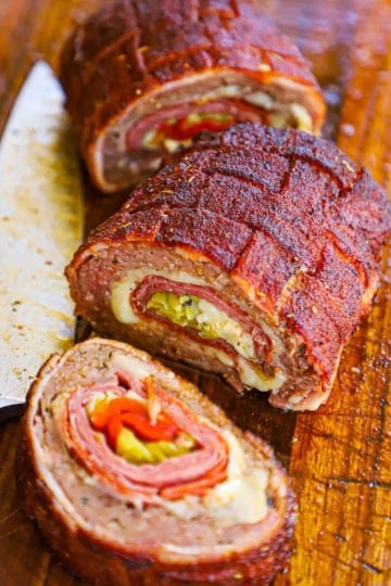 A Smoked Italian Fatty that has been cut into three large pieces revealing the braided topping, and the layers of Italian meat, cheese, and pickled veggies inside.