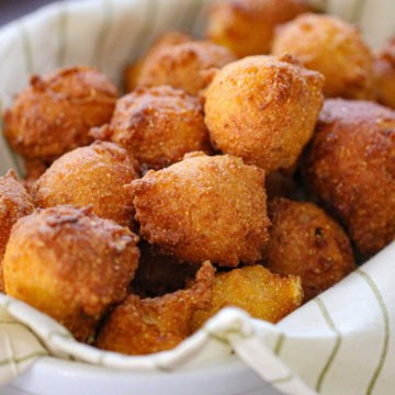 A close-up view of a pile of Traditional Southern Hush Puppies in a basket lined with a striped linen.