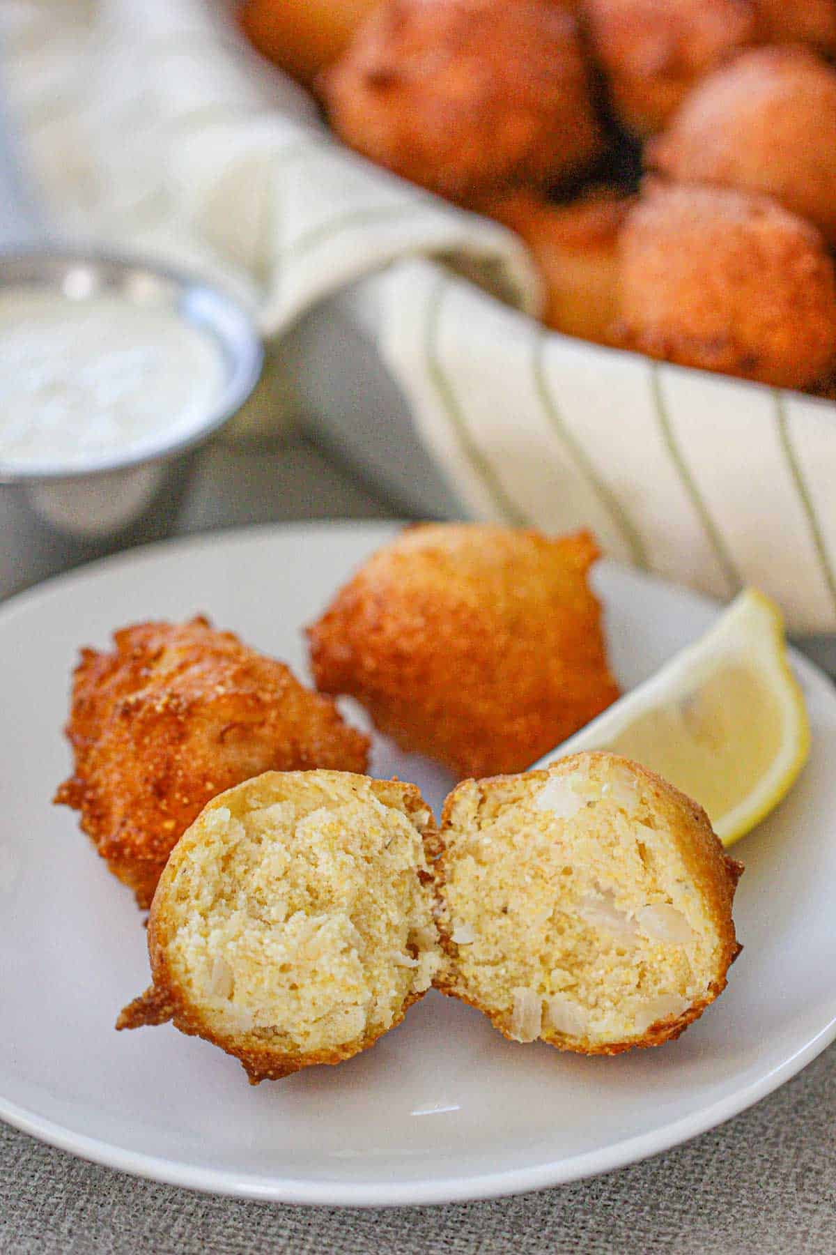 A Traditional Southern Hush Puppy that has been split in half and is sitting next to two more whole hush puppies on a small white plate.