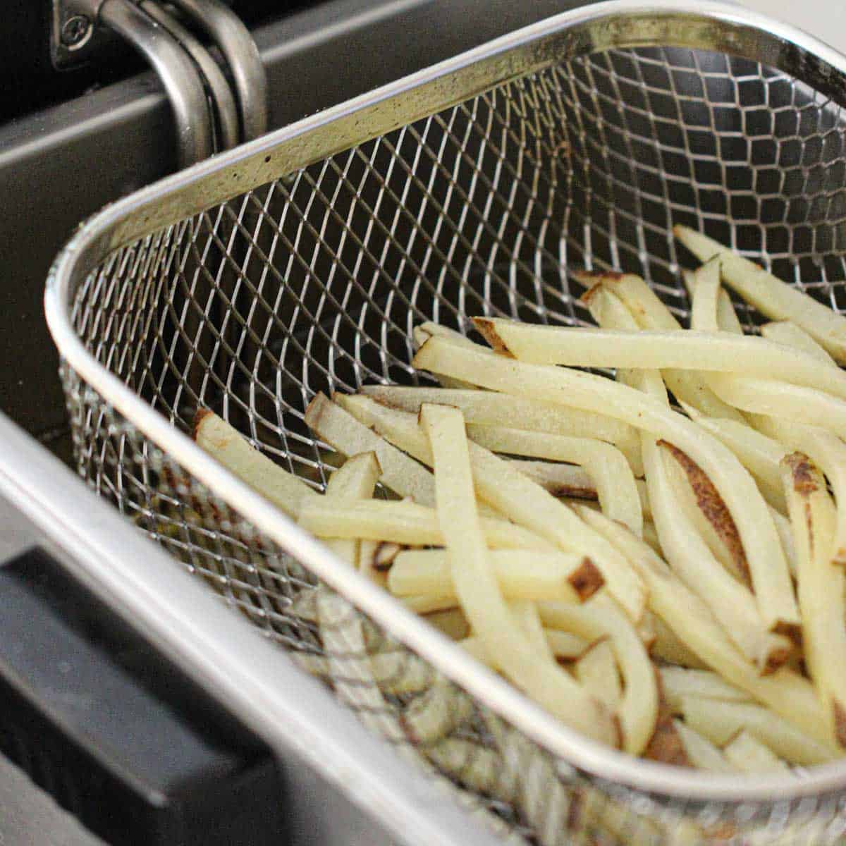 A deep-fryer basked filled with partially fried French fries.