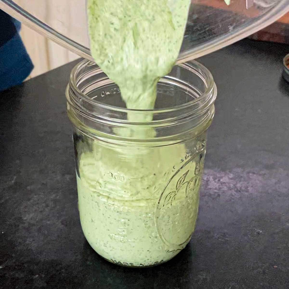 A person pouring homemade Jalapeño-Lime Sauce from a blender into a glass Mason jar.