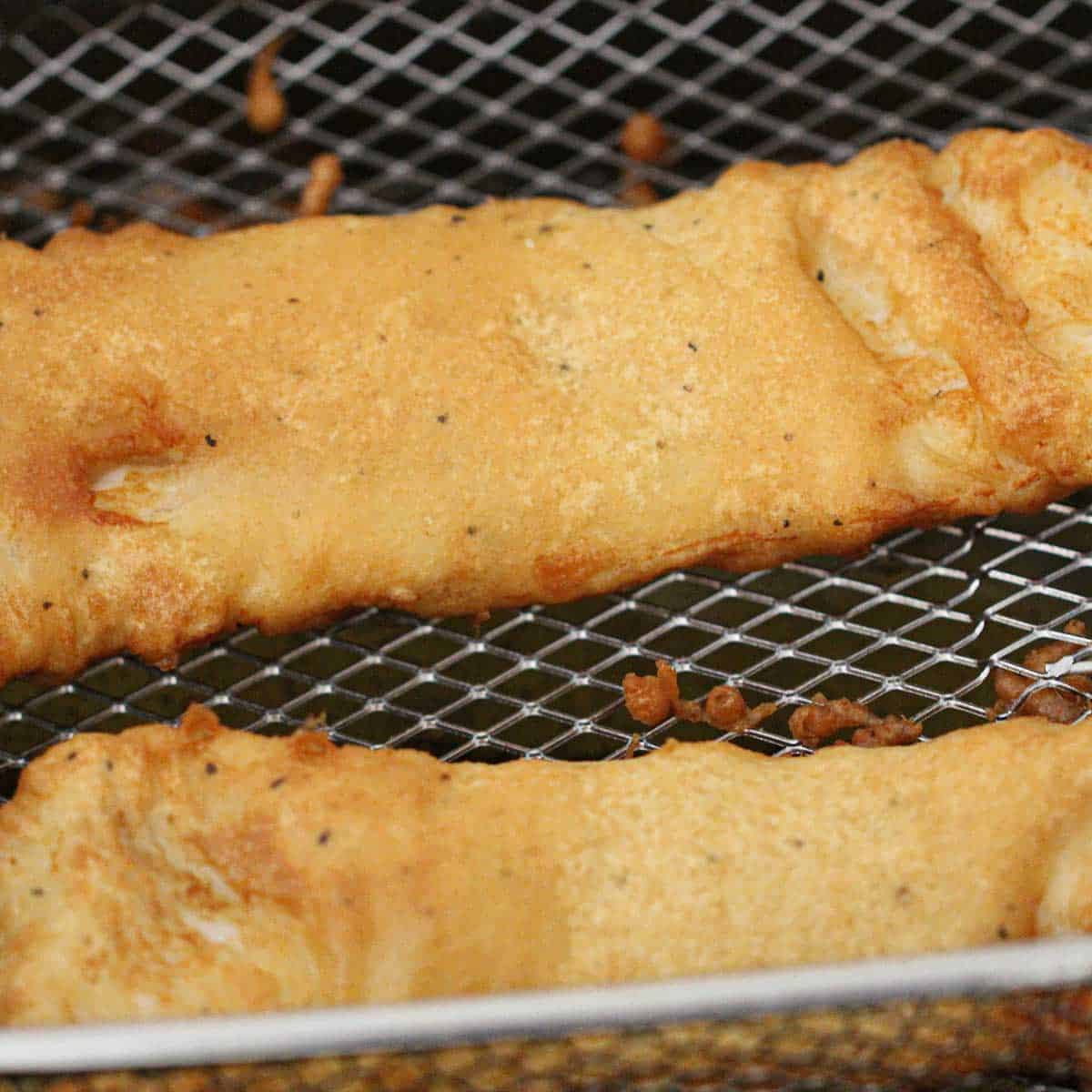 A close-up view of two filets of cod that have been battered and deep-fried and are resting in the deep-fryer basket.