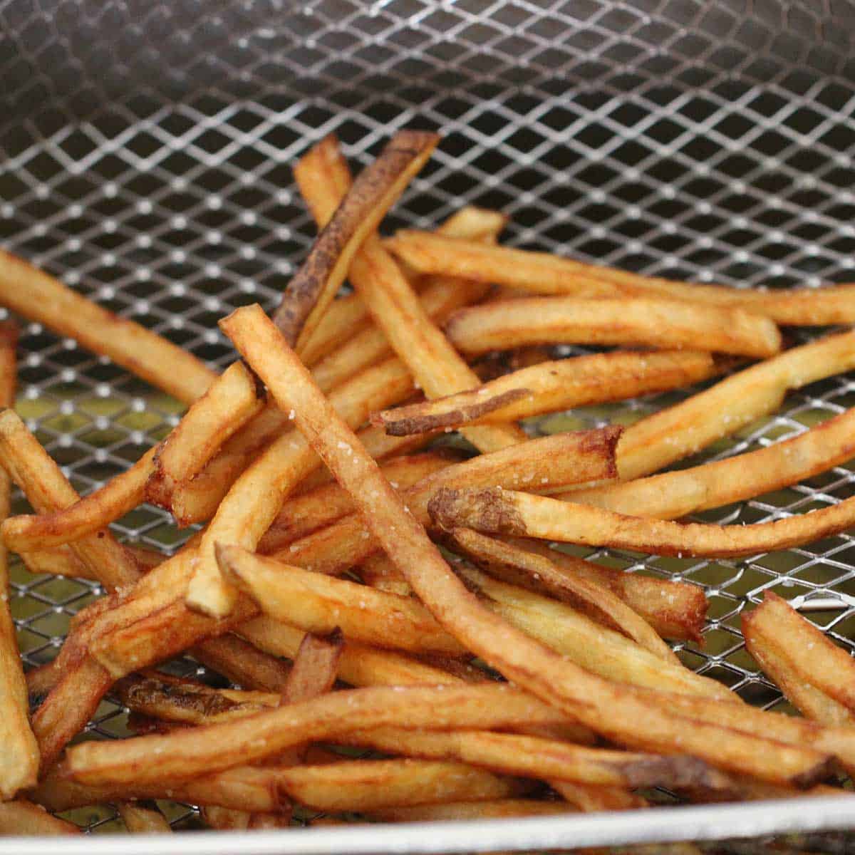 A deep-fryer basket filled with French fries that have just been fried and are golden brown.