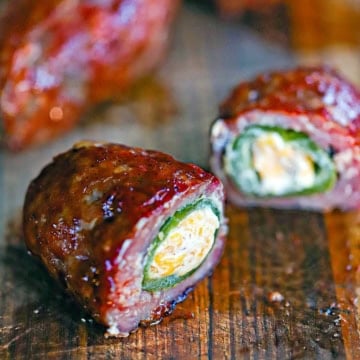 A straight-on view of smoked armadillo eggs on a cutting board with one of them split open to reveal the melty cheese, jalapeño peppers, and sausage encasing it all.