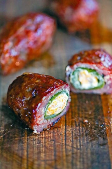 A straight-on view of smoked armadillo eggs on a cutting board with one of them split open to reveal the melty cheese, jalapeño peppers, and sausage encasing it all.