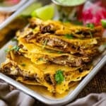 A close-up view of crispy oven baked brisket tacos on a small metal trey with a lime wedge and a small pile of pickled red onions in the rear or the pan.