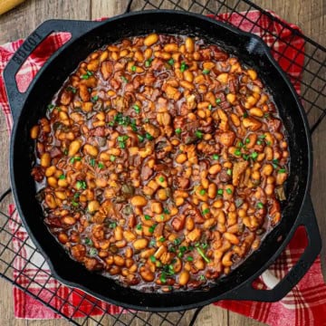 An overhead view of a large black cast-iron skillet filled with freshly prepared Bourbon-Glazed Baked Beans with Pork Belly.