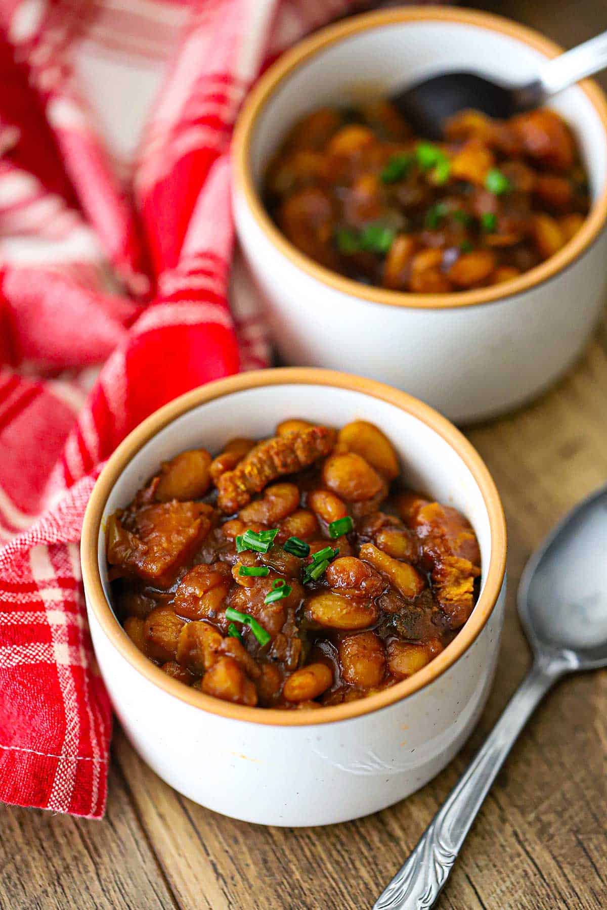 Two small white bowls filled with servings of Bourbon-Glazed Baked Beans with Pork Belly and topped with snipped chives.