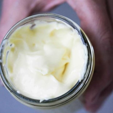 A person holding a glass jar that is filled to the top with homemade mayonnaise.