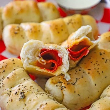 A close-up view of a melt-in-your-mouth pepperoni roll that has been split in half revealing the layers of pepperoni, melted cheese, and flakey dough, resting on top of a row of more pepperoni rolls.