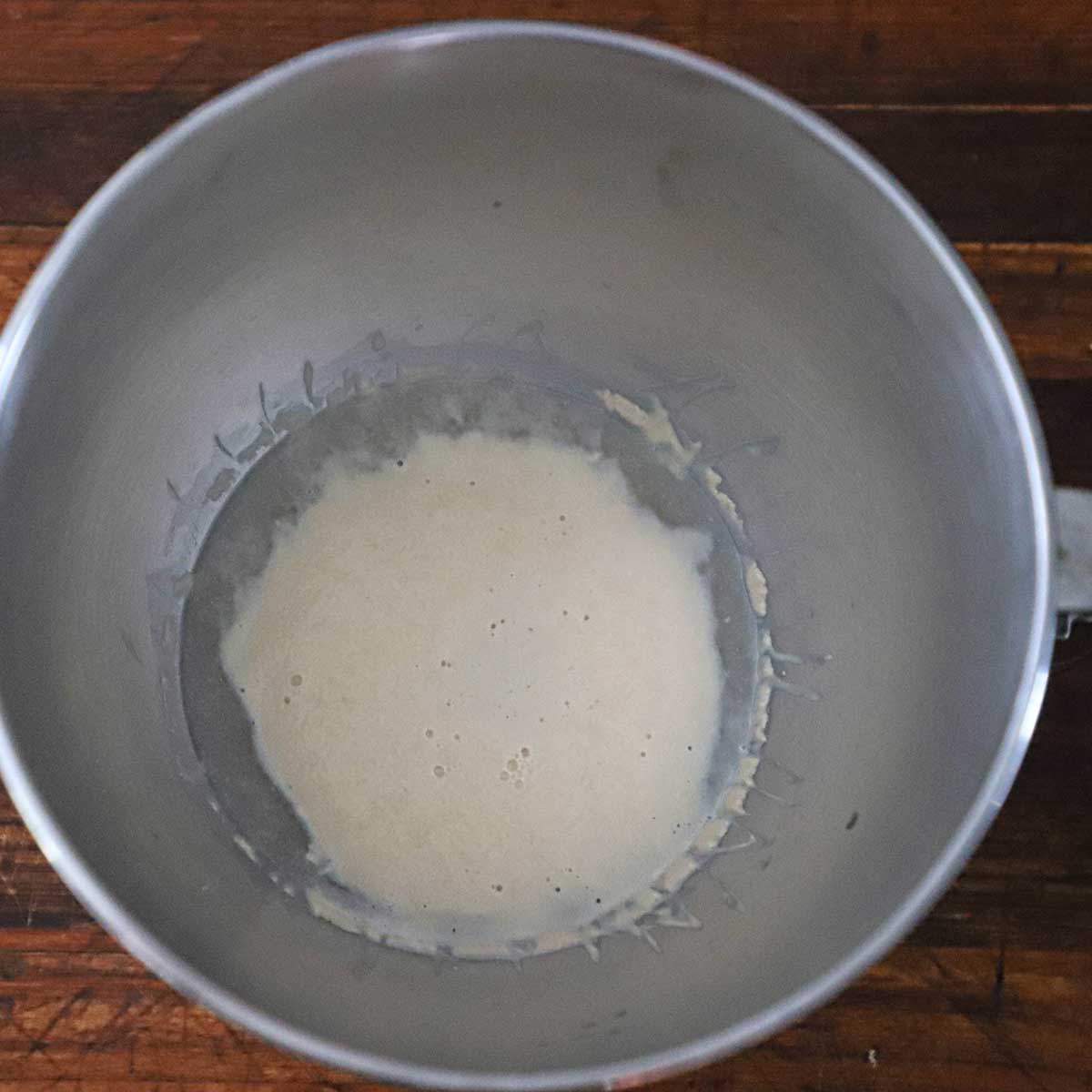 An overhead view of yeast that has activated and is foamy in a mixing bowl with warm water and honey.