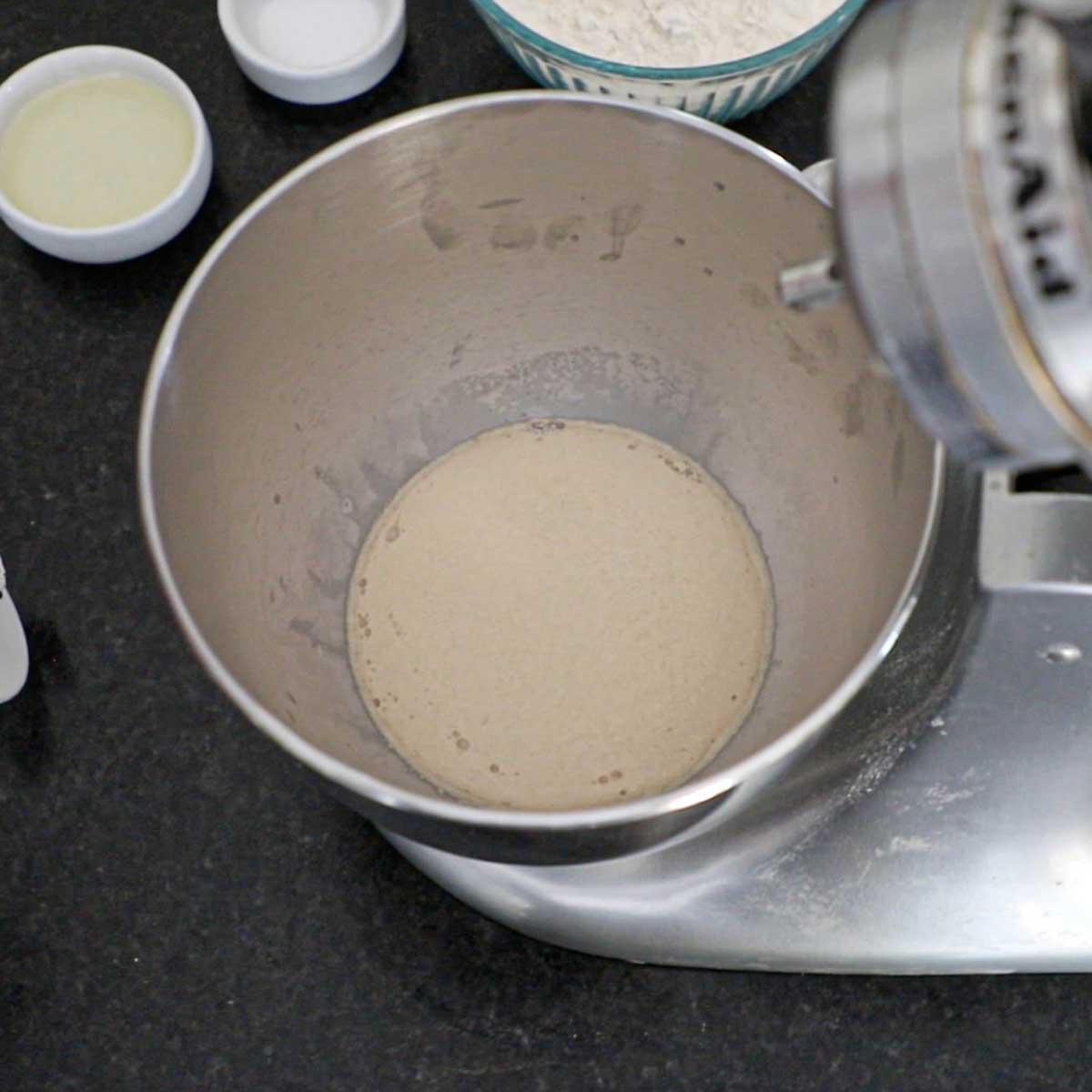 Active yeast that is foaming in warm water with sugar in the bowl of a stand-mixer.