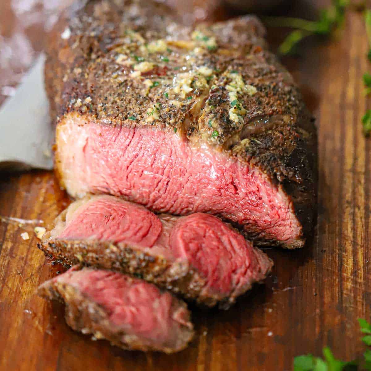 A close-up view of a reverse seared tomahawk steak with bone marrow butter that has two slices cut from it revealing the pink interior meat.