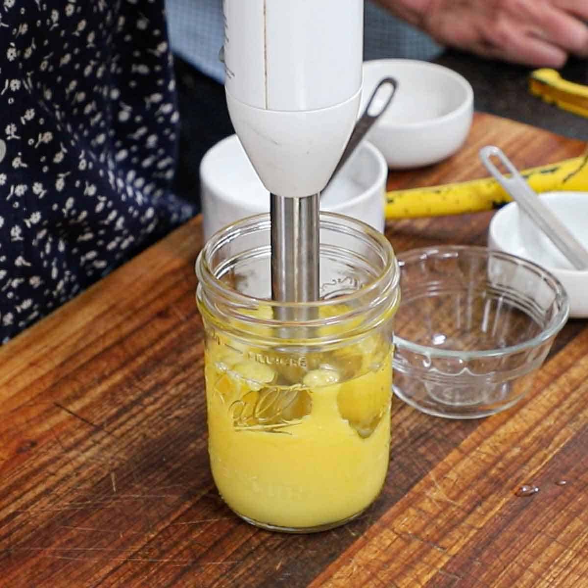 A person using lifting an immersion up and down in a glass jar where has just made homemade mayonnaise.