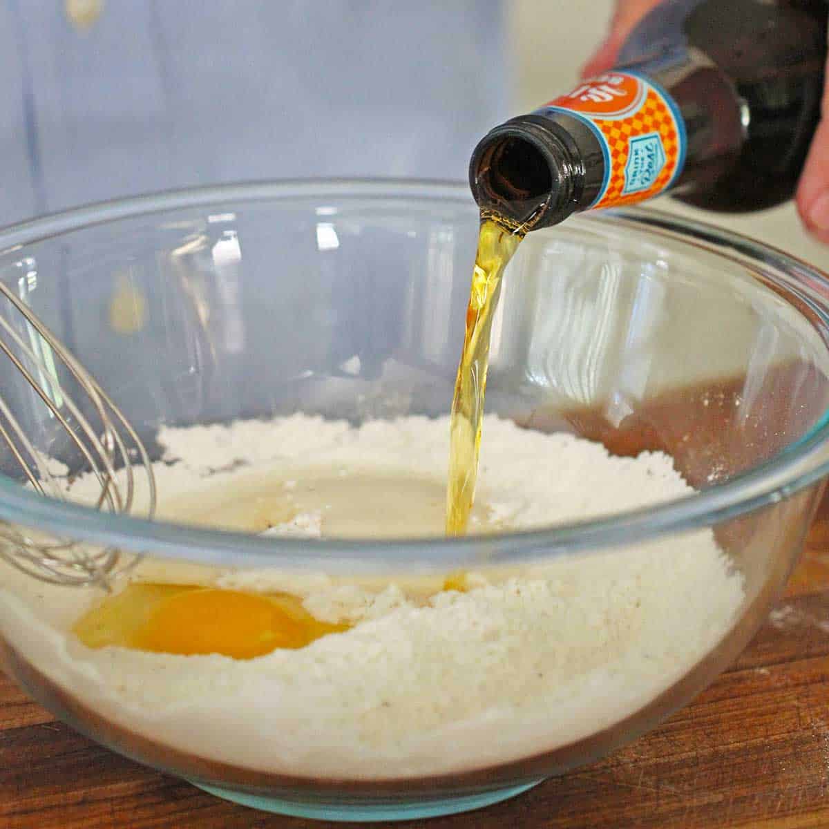 A person pouring beer from a bottle into a bowl filled with the batter for Traditional Southern Hush Puppies.