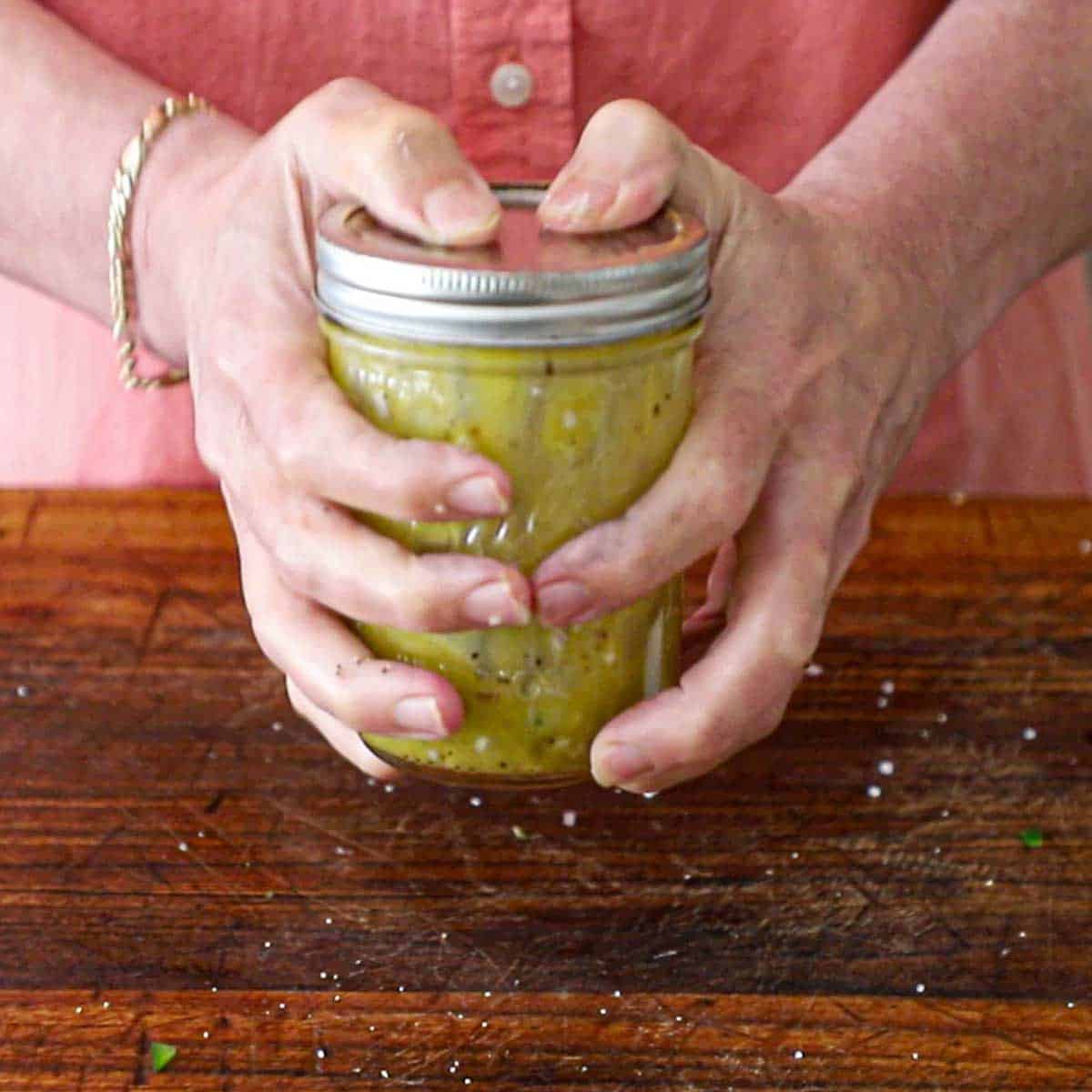 A person using both of his hands to vigorously shake a jar with a lid that contains a homemade citrus-honey vinaigrette.