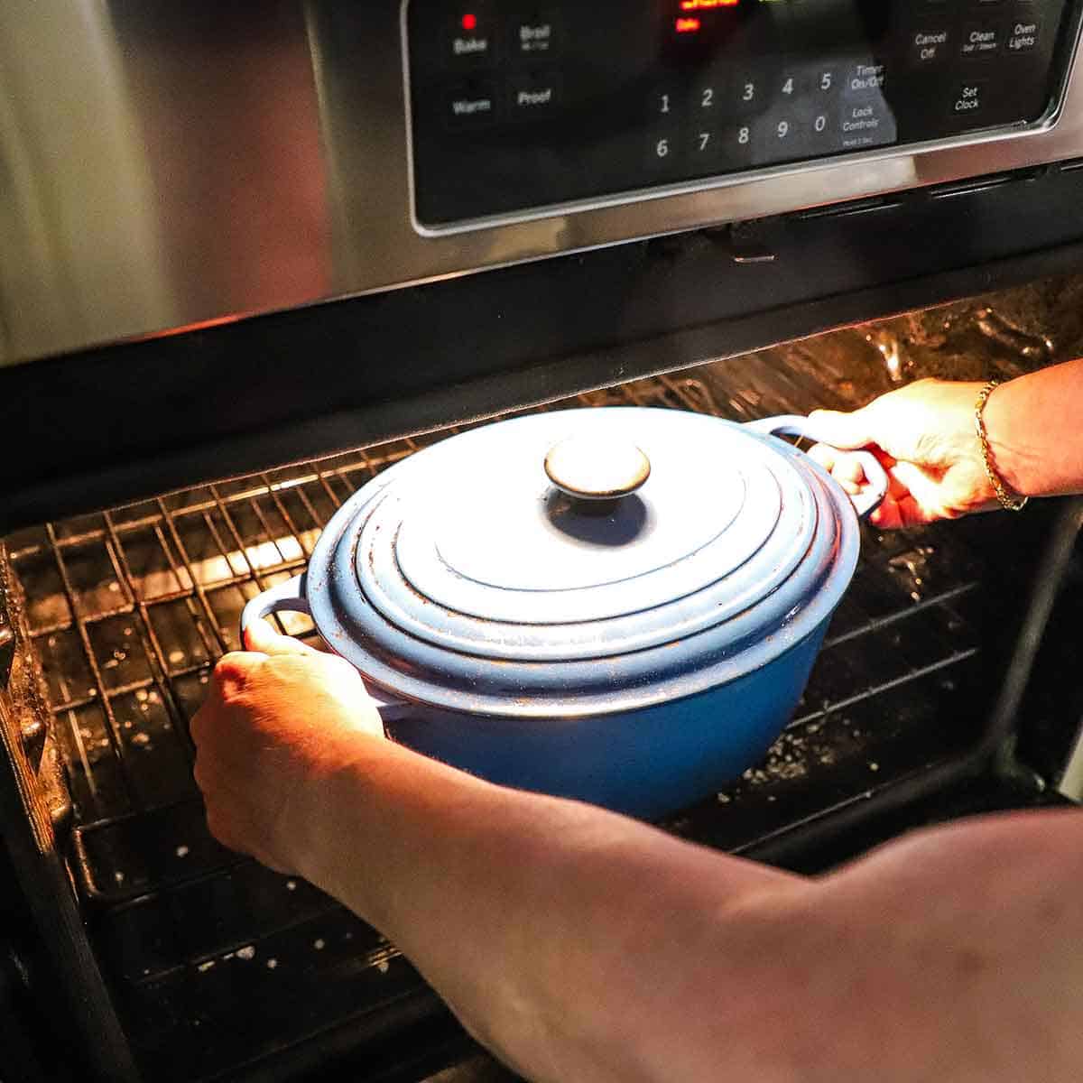 A person placing an oval Dutch oven with a lid on it into an oven.