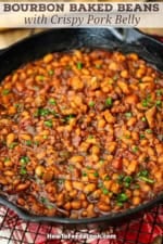 A close-up view of a large black cast-iron skillet filled with freshly prepared Bourbon-Glazed Baked Beans with Pork Belly.