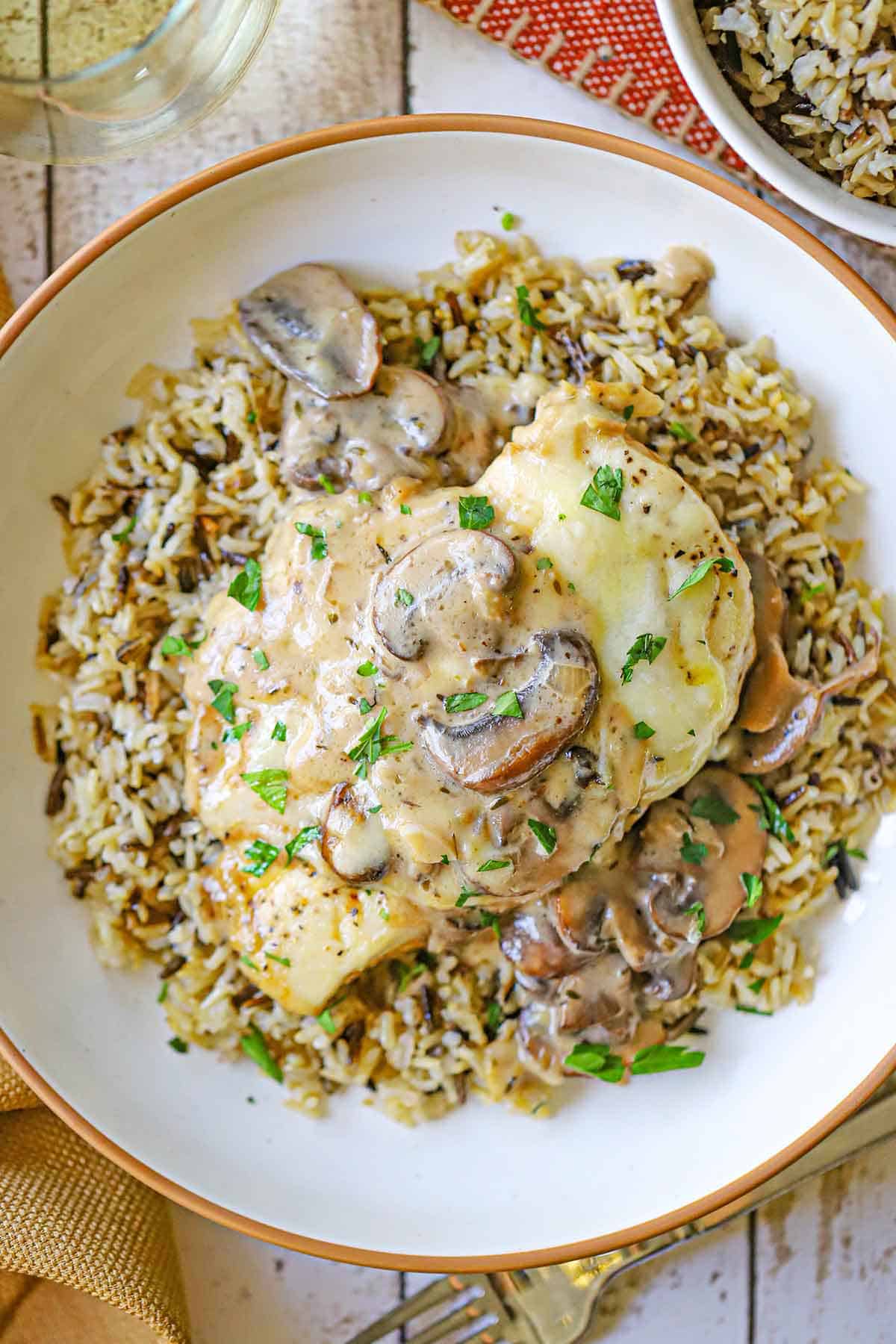 An overhead view of an Elevated Chicken Gloria topped with melty cheese and a creamy mushroom sauce all resting on a bed of cooked wild rice.