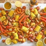 An overhead view a spread of Louisiana Seafood Boil stretching across a white piece of butcher paper with a bowl of drawn butter, a beer bottle, and lemon halves nearby.