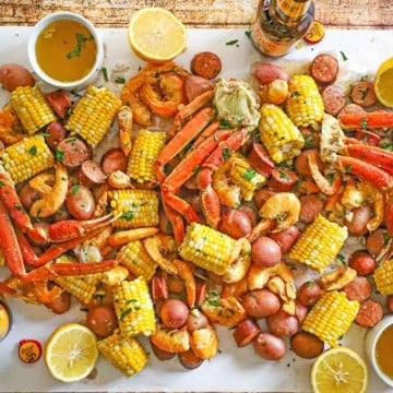 An overhead view a spread of Louisiana Seafood Boil stretching across a white piece of butcher paper with a bowl of drawn butter, a beer bottle, and lemon halves nearby.