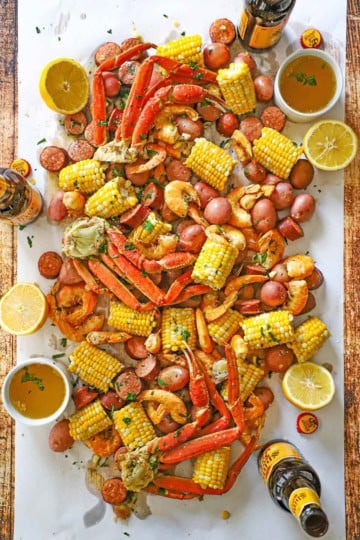 An overhead view a spread of Louisiana Seafood Boil stretching across a white piece of butcher paper with a bowl of drawn butter, a beer bottle, and lemon halves nearby.