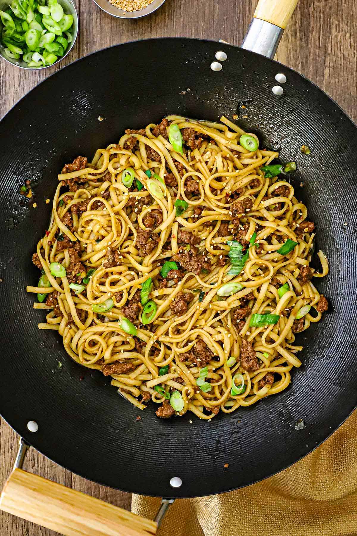 An overhead view of a large wok that is filled with freshly prepared Mongolian Ground Beef Noodles topped with chopped scallions.