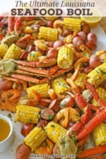 A close-up view a spread of Louisiana Seafood Boil stretching across a white piece of butcher paper with a bowl of drawn butter, a beer bottle, and lemon halves nearby.
