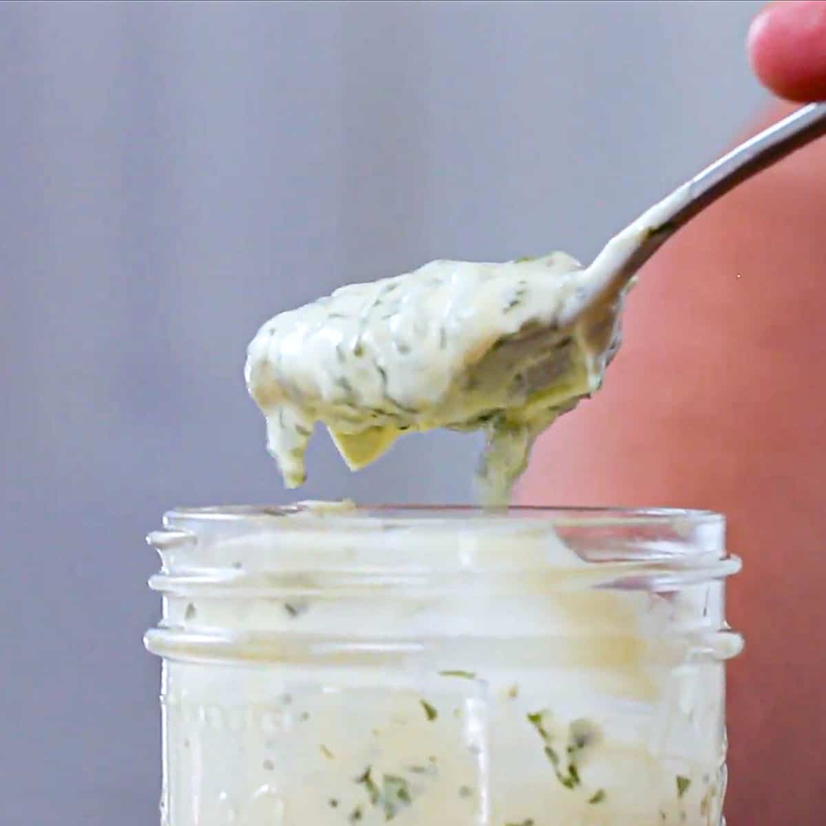 A person using a spoon to lift a serving of homemade garlic basil aioli from a glass jar.