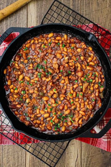 An overhead view of a large black cast-iron skillet filled with freshly prepared Bourbon-Glazed Baked Beans with Pork Belly.