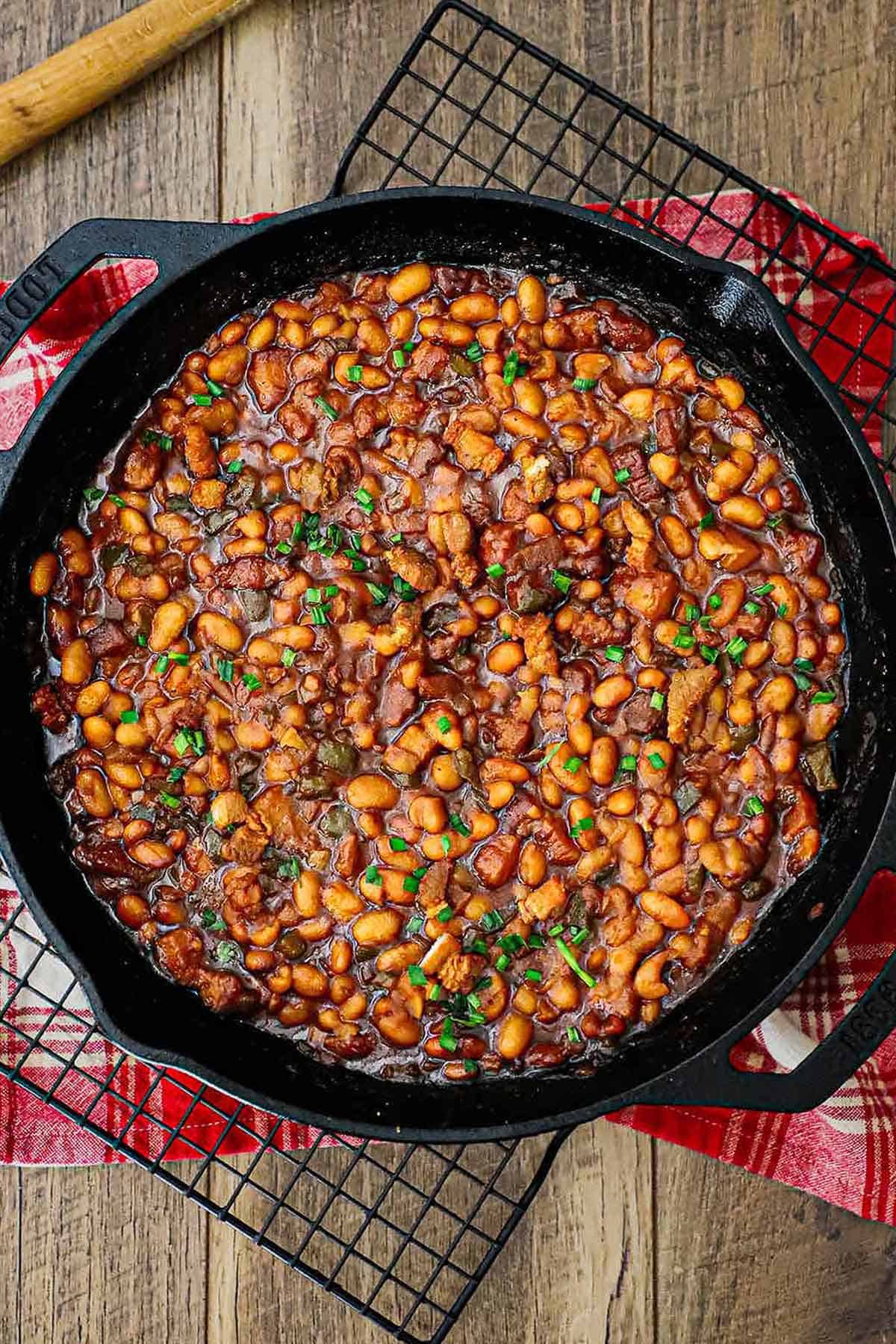 An overhead view of a large black cast-iron skillet filled with freshly prepared Bourbon-Glazed Baked Beans with Pork Belly.