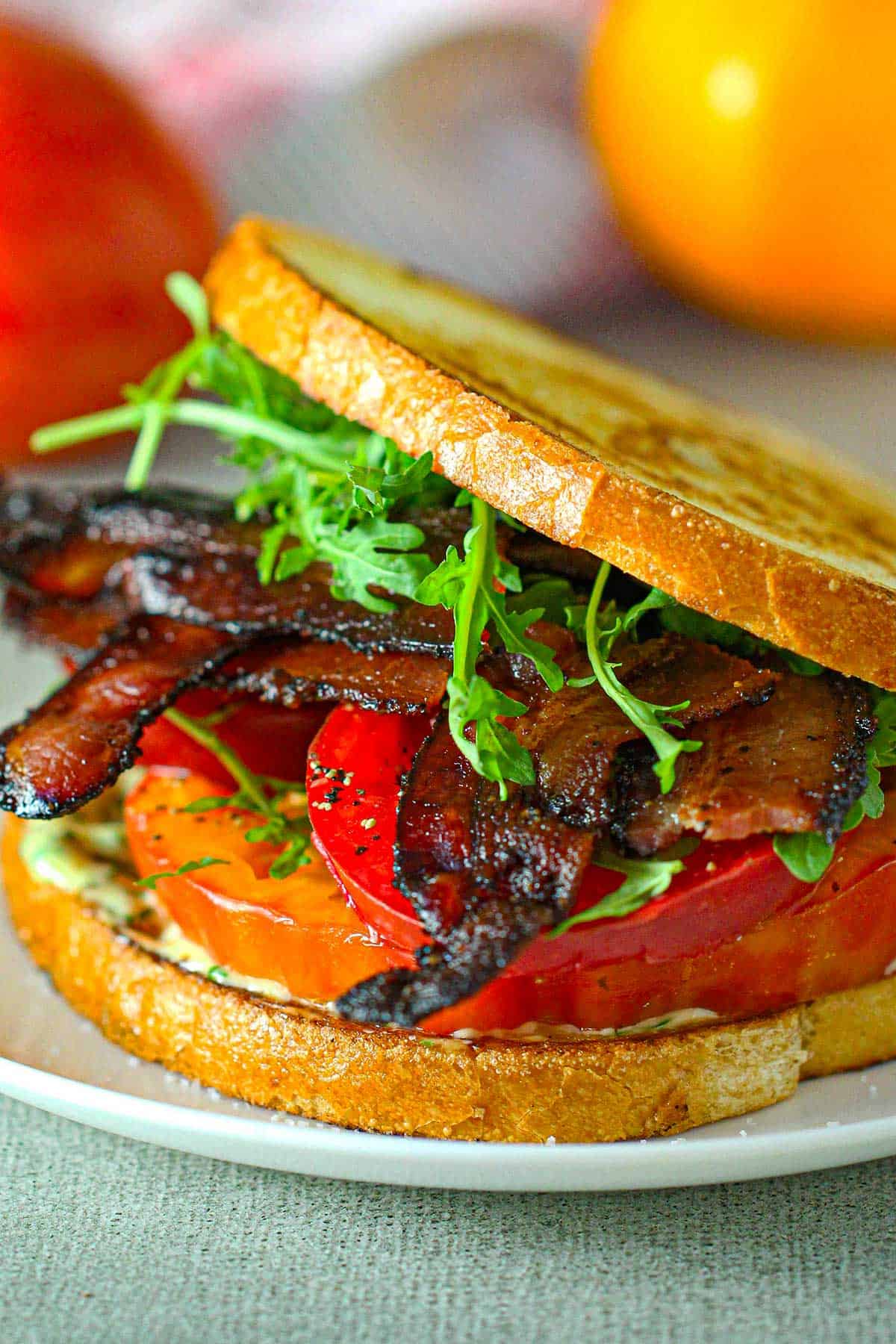 A close-up view of a Classic BLT with Garlic Basil Aioli on lightly toasted sourdough bread on a white plate.