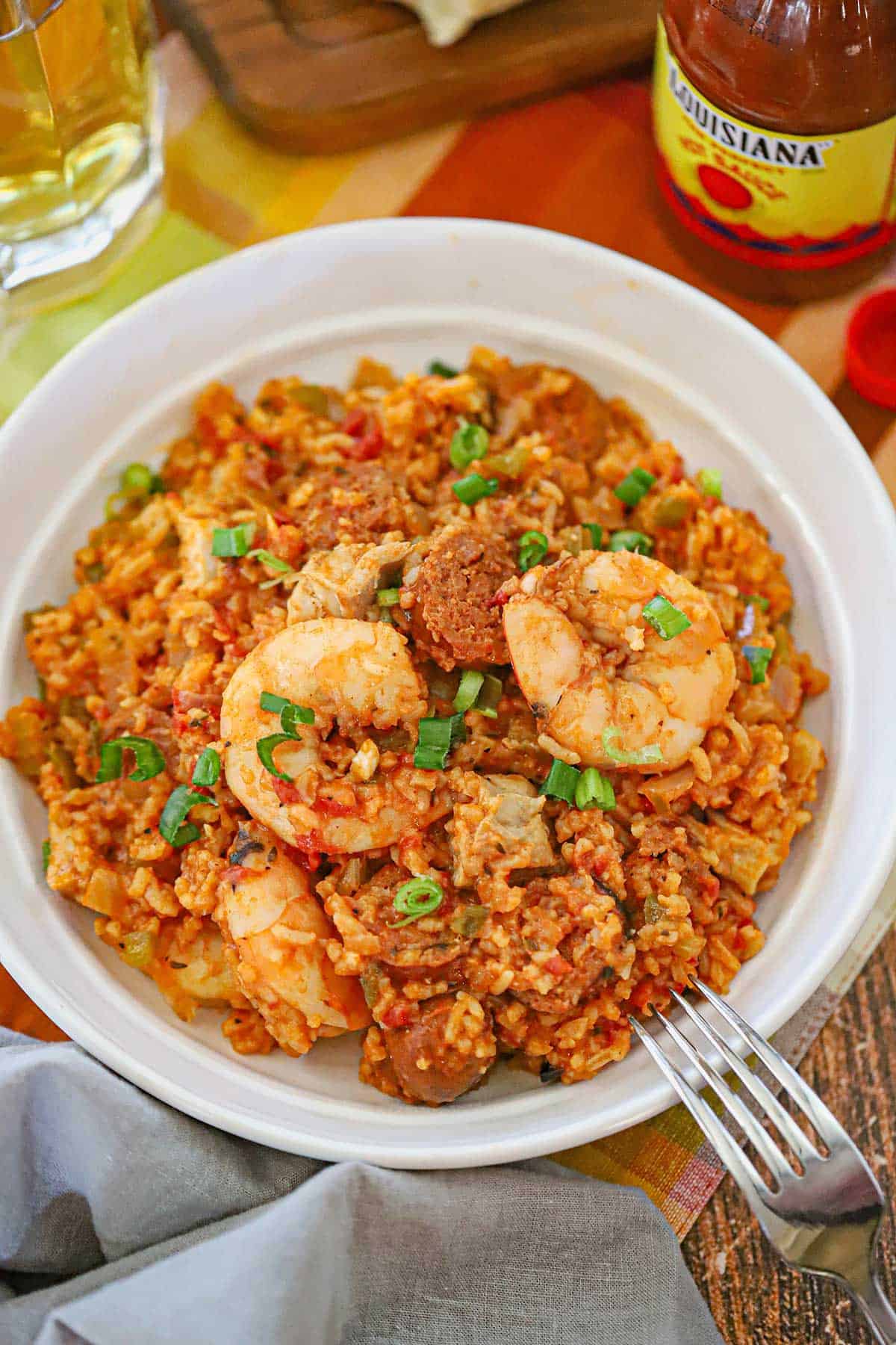 An straight-on view of a white bowl filled with a serving of authentic jambalaya topped with seared shrimp, andouille sausage, and chopped scallions.