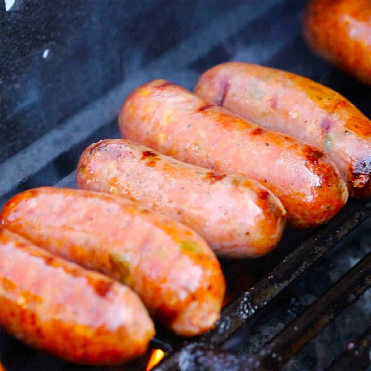 A row of homemade Texas Jalapeño Cheddar Sausage links being grilled on a gas grill.