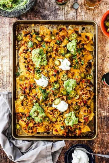 An overhead view of a large serving of Sheet Pan Nachos topped with vegetarian chili, melty cheese, and dollops of sour cream and homemade guacamole.