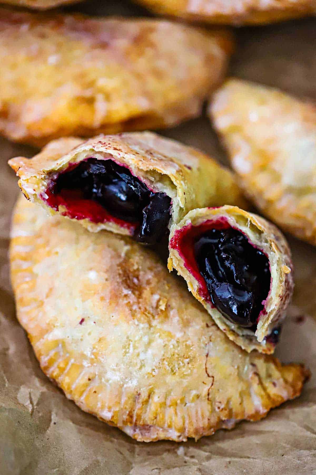 An open cherry filled Southern fried fruit pie that reveals the fruit inside and the two halves are resting on a whole fruit pie.