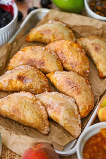 A straight-on view of two rows of Southern Fried Fruit Pies resting on crumpled brown paper nestled into a rectangular baking pan.