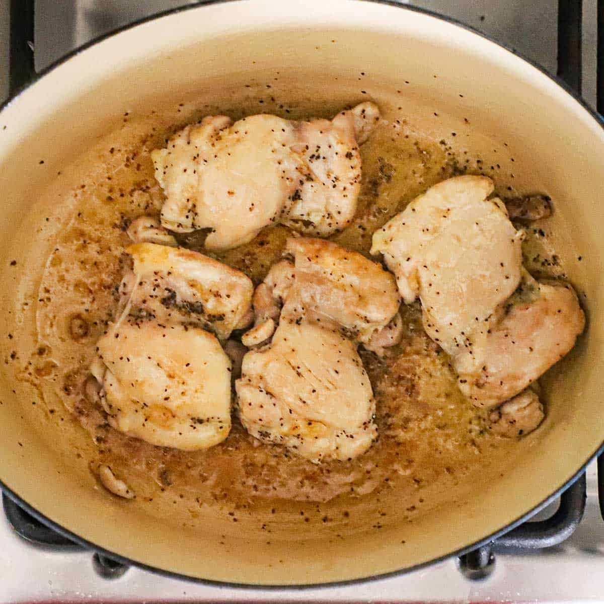 Four boneless seasoned chicken thighs being seared in a large Dutch oven on a gas stove.